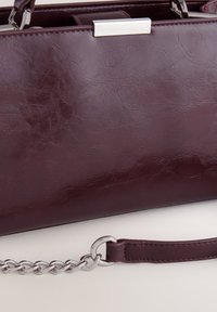 Rožnato rdeča torbica iz umetnega usnja z gladko teksturo, srebrnimi kovinskimi dodatki, verižnim trakom in oblikovano pravokotno obliko.