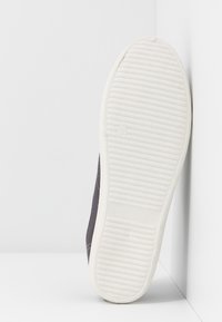 Baskets gris foncé avec une semelle en caoutchouc texturée et des accents blancs. La semelle présente un motif pour une meilleure adhérence. Design plat et minimaliste.
