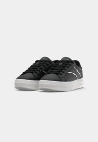 Zapatillas negras hechas de un material texturizado con una suela de goma blanca. Presentan cordones negros y un detalle de diseño en blanco en los laterales.