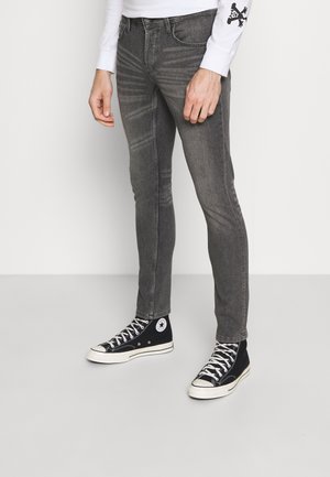 Jeans justos cinzentos feitos de denim, com uma textura subtil e detalhes de desgaste, combinados com ténis de cano alto pretos com detalhes brancos.