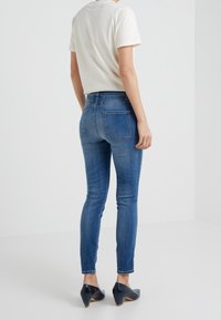 Vaqueros ajustados de mezclilla en color azul, con una cintura alta, diseño de cinco bolsillos y un ligero desgastado. Combinados con una camiseta blanca básica.