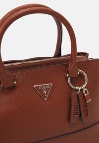 Sac à main texturé marron avec deux poignées, quincaillerie dorée et un logo triangulaire. Comprend une fermeture éclair et des étiquettes attachées avec des numéros.