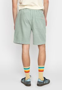 Groene corduroy shorts met een elastische tailleband, een achterzak en een gestructureerd oppervlak. Gemaakt in combinatie met kleurrijke gestreepte sokken en sneakers.