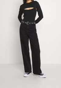 Haut noir à manches longues et côtelé avec un détail découpé, associé à un jean large noir taille haute et des baskets noires à semelles blanches.