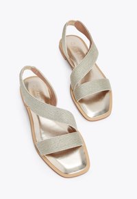 Sandali metallici dorati con schiena aperta, cinghie intrecciate a incrocio, punta quadrata e suola piatta con una leggera texture.