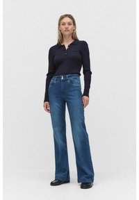 Marinblå ribbad långärmad topp med krage, ihop med utsvängda blå denimjeans som har två framknappar och fickor.