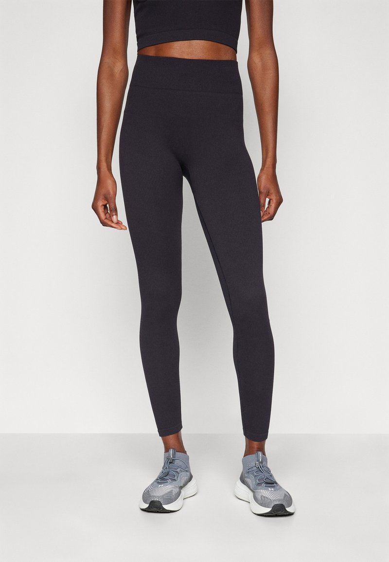 Leggings neri a coste con vita alta, caratterizzati da una texture liscia. Abbinati a sneakers sportive grigie per un look completo.