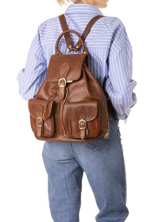 Zaino in pelle marrone con cinghie a fibbia indossato da una persona con camicia a righe blu e jeans, visto da dietro.