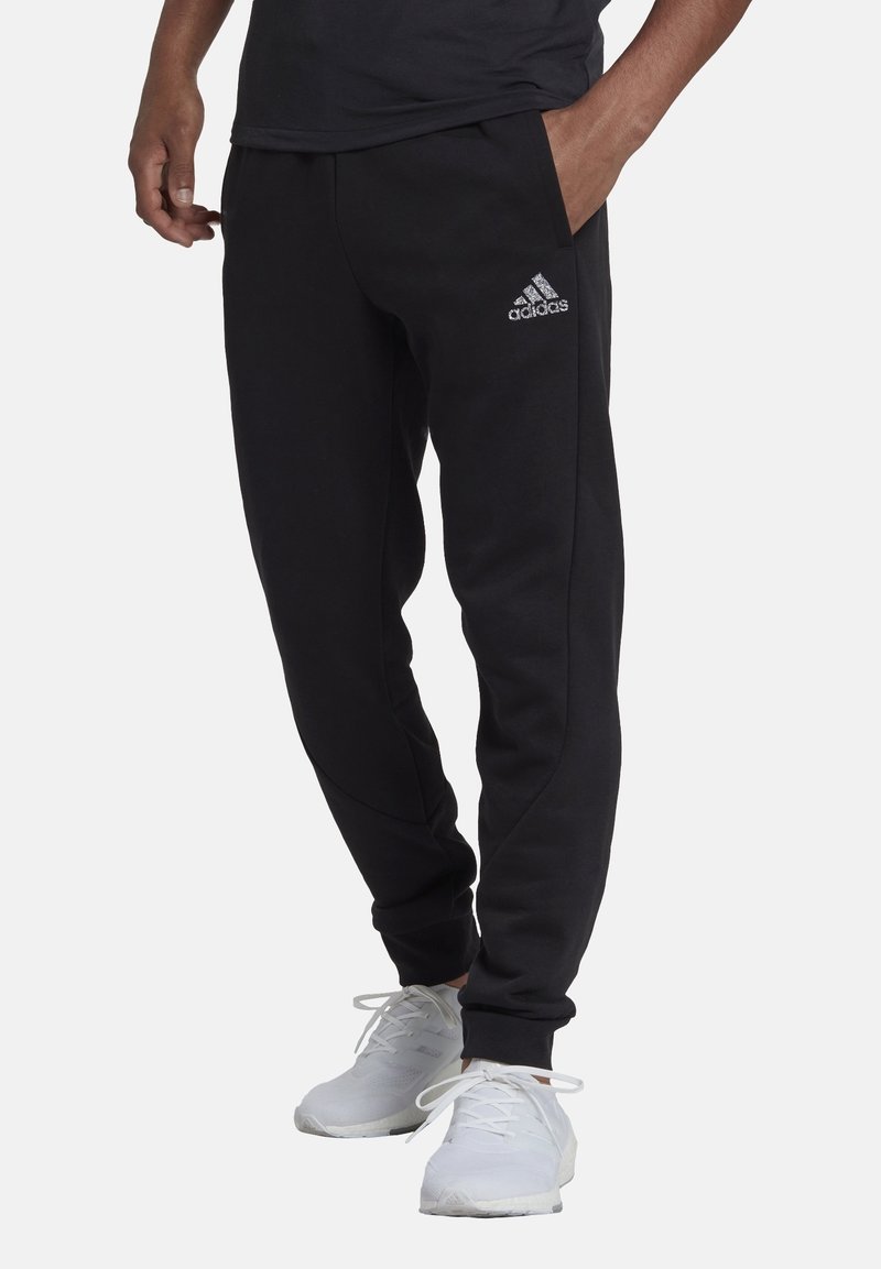 Svarta träningsbyxor i mjukt material, med sidofickor och smal passform, prydda med en silverfärgad Adidas-logotyp på vänster lår.