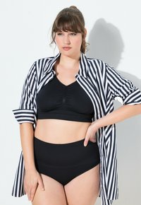 Schwarzer Bralette und hochgeschnittene Unterteile kombiniert mit einem schwarz-weißen gestreiften Hemd. Das Hemd hat aufgerollte Ärmel und Knopfdetails.