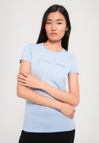 Lichtblauw katoenen T-shirt met korte mouwen. Heeft een cursieve "Armani Exchange"-logo geborduurd in een iets donkerder blauw.