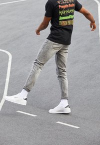 Grå denimjeans med smal passform, ihop med vita sneakers och ribbade vita strumpor, bärs med en svart grafisk T-shirt.