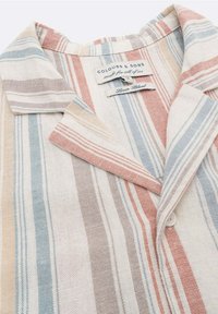 Collo di camicia di lino con bottoni, a righe verticali in tonalità pastello di beige, blu e rosa, con etichetta del marchio "Colours & Sons".
