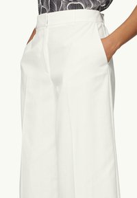 Pantaloni bianchi su misura con vita alta, tasche laterali e un tessuto liscio e leggero. Il design è pulito e strutturato.