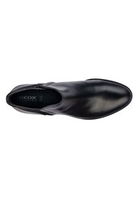 Stivale alla caviglia in pelle nera con una texture liscia, punta rotonda, chiusura con zip laterale e un sottile dettaglio di cucitura lungo la suola.