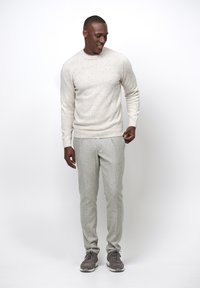 Hellgrauer, gestrickter Pullover mit gesprenkelter Textur, kombiniert mit hellgrauen taillierten Hosen und grauen Sportschuhen.