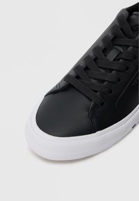 Μαύρο δερμάτινο sneakers με στρογγυλή μύτη, υφασμάτινη επιφάνεια και επ ίπεδη άσπρη καουτσούκ σόλα. Διαθέτει μαύρες κορδόνες και ελάχιστη φωτογραφία.