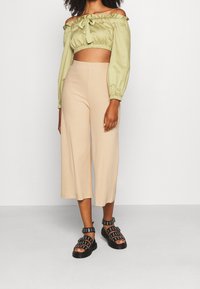 Top cropped olive vert à épaules dénudées avec un col noué, associé à un pantalon large beige à côtes et des sandales noires à lanières.