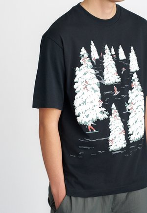 Sort T-shirt med en vinterscene med sneklædte fyrretræer og små skiløbere og snowboardere blandt træerne.