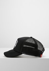 Gorra de béisbol negra con un panel frontal sólido, espalda de malla y visera curva. Presenta un parche de logo blanco y una etiqueta de acento roja en el lateral.