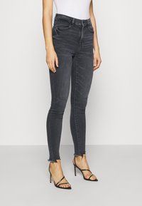 High-waisted, slim-fit black jeans with a faded texture and raw hemline, paired with black strappy high-heeled sandals.