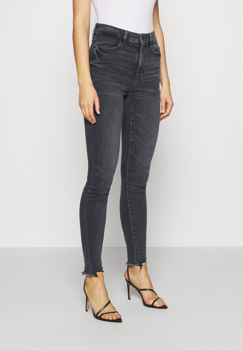 High-waisted, slim-fit black jeans with a faded texture and raw hemline, paired with black strappy high-heeled sandals.