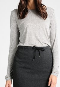 Long-sleeve top in light silver fabric with textured finish, paired with a dark gray skirt featuring a drawstring waistband and smooth texture.