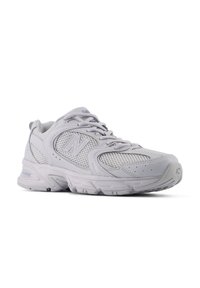 Scarpa atletica grigio chiaro con tomaia in mesh, suola in gomma, colletto imbottito e logo visibile. Presenta una punta arrotondata e cuciture rinforzate.