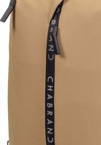 Sac à dos marron avec une surface texturée, doté d'une fermeture éclair noire et d'une sangle de marque. Le design comprend une silhouette moderne et épurée.