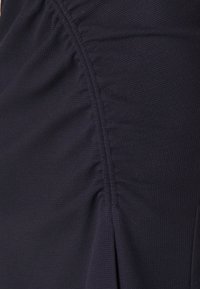 Marinblått tyg med strukturerad, ribbad yta; har samlade detaljer och veck längs sidan, vilket skapar subtil dimension och flöde.