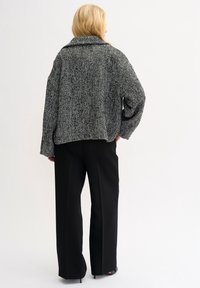 Herringbone-mönstrad, överdimensionerad svart och vit jacka med en bred krage, tillsammans med svarta vida byxor. Slät tygtextur.