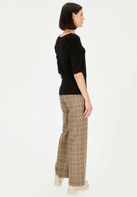 Czarna bluzka z rękawami trzy czwarte i marszczeniem na ramionach. Brązowe spodnie w kratę o szerokich nogawkach i masywne beżowe buty.