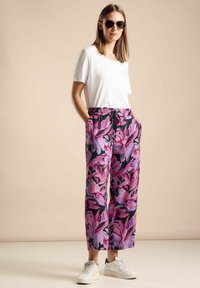 Relaxed-fit witte t-shirt, bloemenpatroon in roze en paars wijdvallende broek met elastische tailleband, gecombineerd met witte sneakers en een zonnebril.