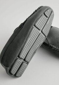 Chaussures à enfiler en tissu gris avec un matériau texturé, semelle en caoutchouc plate présentant des motifs en zigzag et un design ajusté et sans couture.