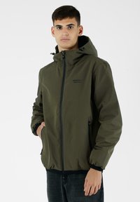 Giacca verde oliva con cappuccio, chiusura frontale con zip e polsini elasticizzati. Presenta un logo sul petto e tasche laterali con zip.