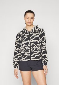 Hættetrøje med lynlås i sort og beige zebra mønster, med lange ærmer, raglan-design og ribbede manchetter. Kombineret med sorte shorts.