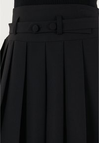 Jupe plissée noire avec une texture lisse, une taille ajustée avec deux boutons ronds, et un détail de ceinture en tissu assorti.