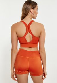 Oranžová sportovní podprsenka a odpovídající šortky vyrobené z elastické tkaniny, s designem racerback a výřezem na zadní straně.