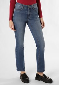 Blauwe denim jeans met een hoge taille, taps toelopende broekspijpen en een licht rafelrandje; gecombineerd met zwarte platform loafers. Met voorzakken.