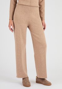 Pantaloni beige a gamba larga realizzati in morbido tessuto a maglia con vita elastica. Abbinati a scarpe da ginnastica marroni per un look casual.