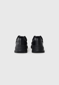 Black athletic shoes with a sleek design, made of synthetic material. Features textured details and a thick sole for support.