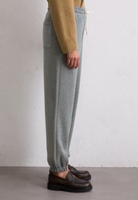 Grijze sweatpants met elastische boorden, gemaakt van zacht materiaal. Voorzien van een zijzak en een verstelbare trekkoord tailleband.