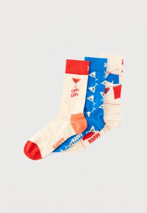 Trois chaussettes colorées avec des motifs sur le thème des cocktails : verres à martini, linge étendu sur une corde à linge et texte "cin cin" sur un fond blanc.
