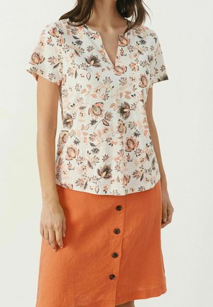Woman wearing a short-sleeve floral blouse with a V-neck and an orange button-front skirt.