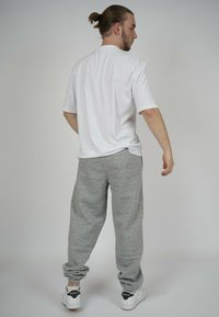 White short-sleeve t-shirt and gray sweatpants with an elastic waistband. Model wears white sneakers with black accents.
