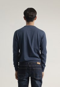 Suéter de punto azul marino con cuello redondo, mangas largas y dobladillo ajustado, combinado con jeans azul oscuro que tienen bolsillos traseros y una etiqueta de cuero.