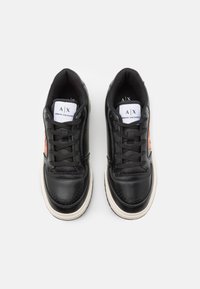 Svarta lädersneakers med en slät yta, utrustade med en vit och röd logotypetikett, rund tå, vadderad krage och en krämfärgad yttersula.