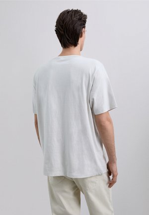 Camiseta de algodón de color gris claro con un corte relajado, mangas cortas y un escote redondeado, con una textura lisa y sin patrones visibles.