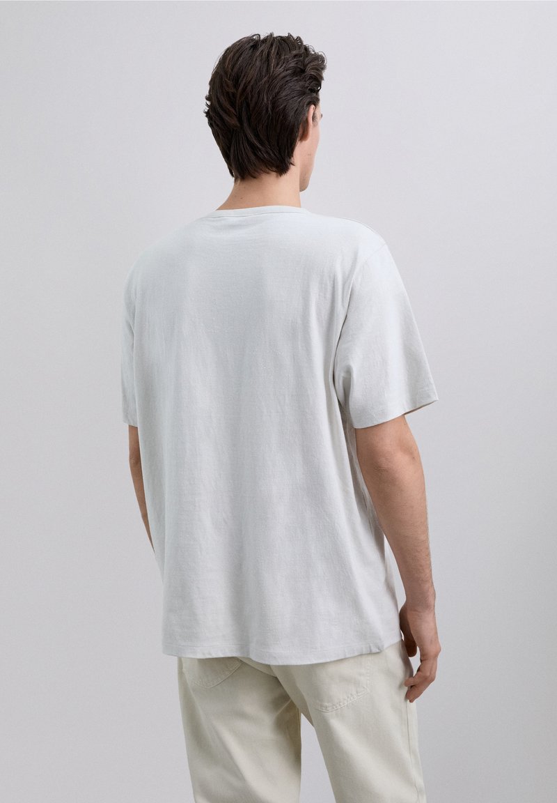 Jasnoszary bawełniany t-shirt o luźnym kroju, z krótkimi rękawami i okrągłym dekoltem, z gładką fakturą i bez widocznych wzorów.