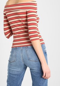 Rød og beige stribet off-the-shoulder top med lange ærmer, parret med lyseblå højtaljede jeans med en falmet tekstur og lommer.